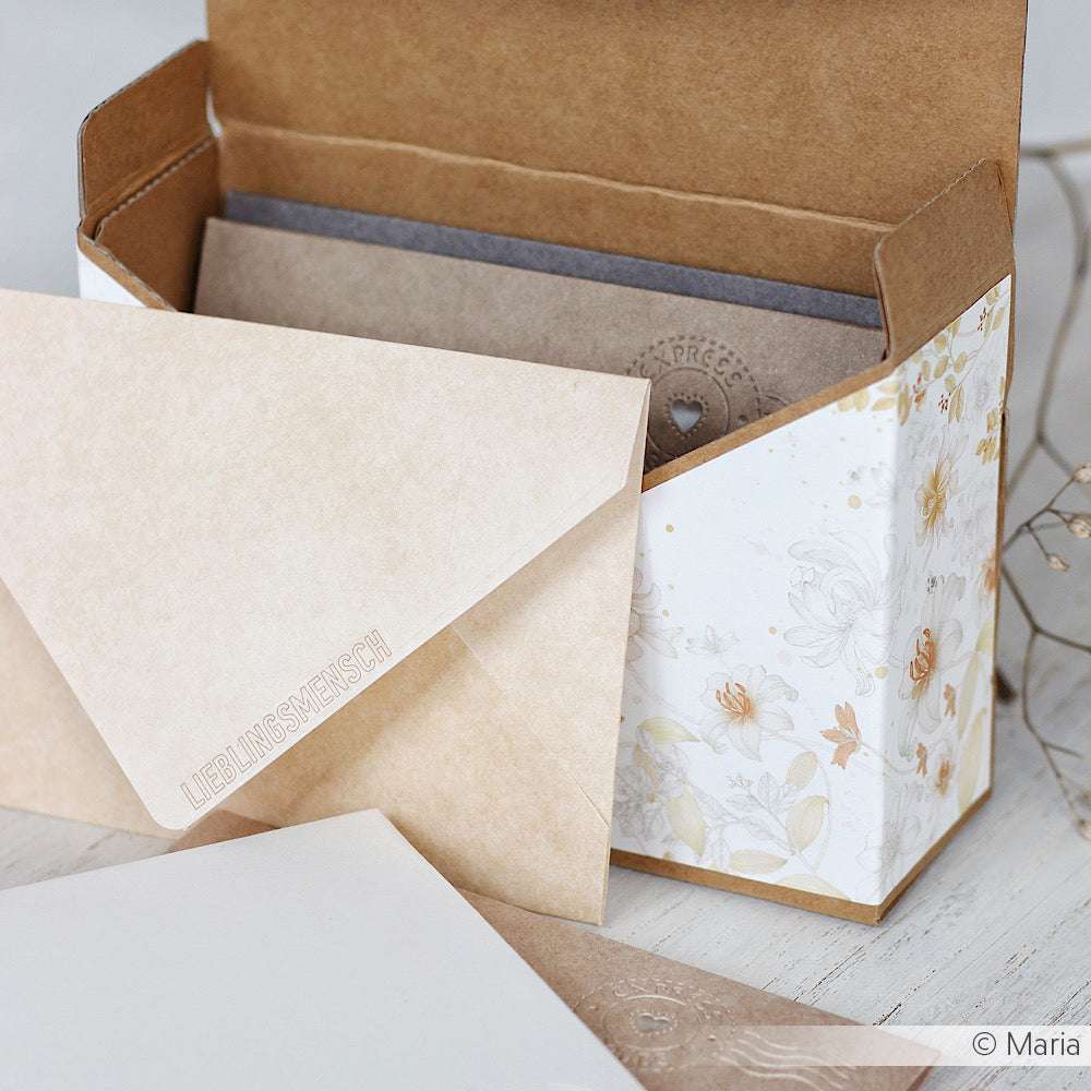 Eine ☆ Aufbewahrungsbox mit cremefarbenen Umschlägen und blumengemusterten Karten steht auf einem hellen Tisch.