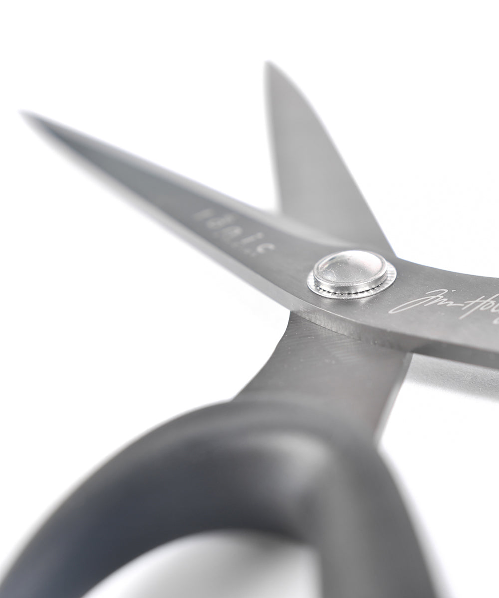 Nahaufnahme einer geöffneten Schere mit schwarzem Griff auf weißem Hintergrund.