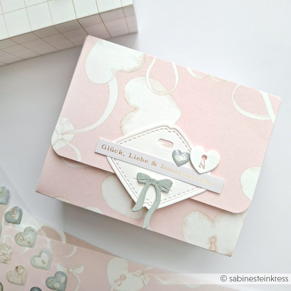 Ein rosafarbener Geschenkumschlag von Alexandra Renke, verziert mit Herzen und Schleifen und der Aufschrift "Glück, Liebe & Sonnenschein" - ideal zum Basteln von Karten oder zum Aufkleben von Herzen.