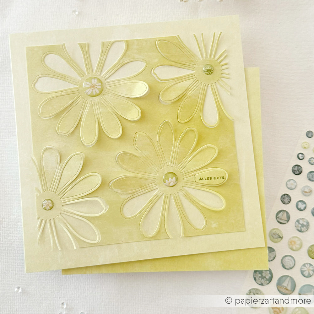 Eine hellgelbe Karte von Alexandra Renke mit drei großen geprägten Gänseblümchen, dezenten Akzenten aus Sticker Dots und einem kleinen „ALLES GUTE“-Schriftzug – ideal für die kreative Kartengestaltung.