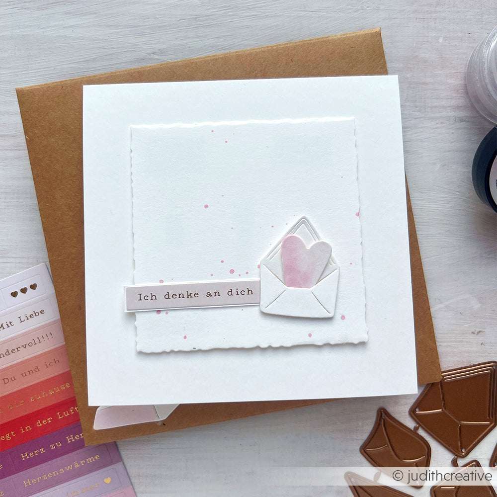Handgefertigte Alexandra Renke Karte mit kleinem Umschlag und Herz, ideal zur Kartengestaltung. Mit der Aufschrift "Ich denke an dich" auf einem weißen Quadrat, elegant verziert mit dezenten Sticker-Streifen.