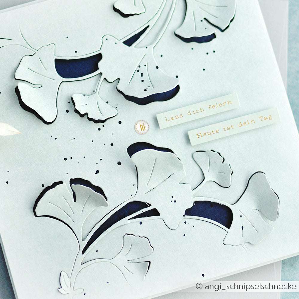 Weiße Karte von Alexandra Renke mit Ginkgo-Blatt-Ausschnitten, Verzierung durch Sticker-Streifen, blauem Hintergrund und deutschem Text "Lass dich feiern" & "Heute ist dein Tag" - ideal für kreative Anlässe.