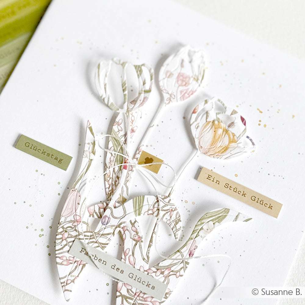 Zarte Papiertulpen mit floralen Mustern zieren eine weiße Karte von Alexandra Renke, die mit deutschen Textaufklebern, dezenten Farbspritzern und kreativer Kartengestaltung für einen stilvollen Touch sorgt.