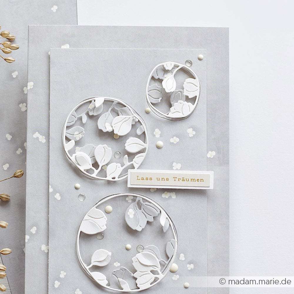 Handgemachte Karte von Alexandra Renke mit weißen Blumenkreisausschnitten, einem weichen grauen Hintergrund und dem Text "Lass uns Träumen" - perfekt für die Kartengestaltung oder zum Verzieren mit Aufkleberstreifen.