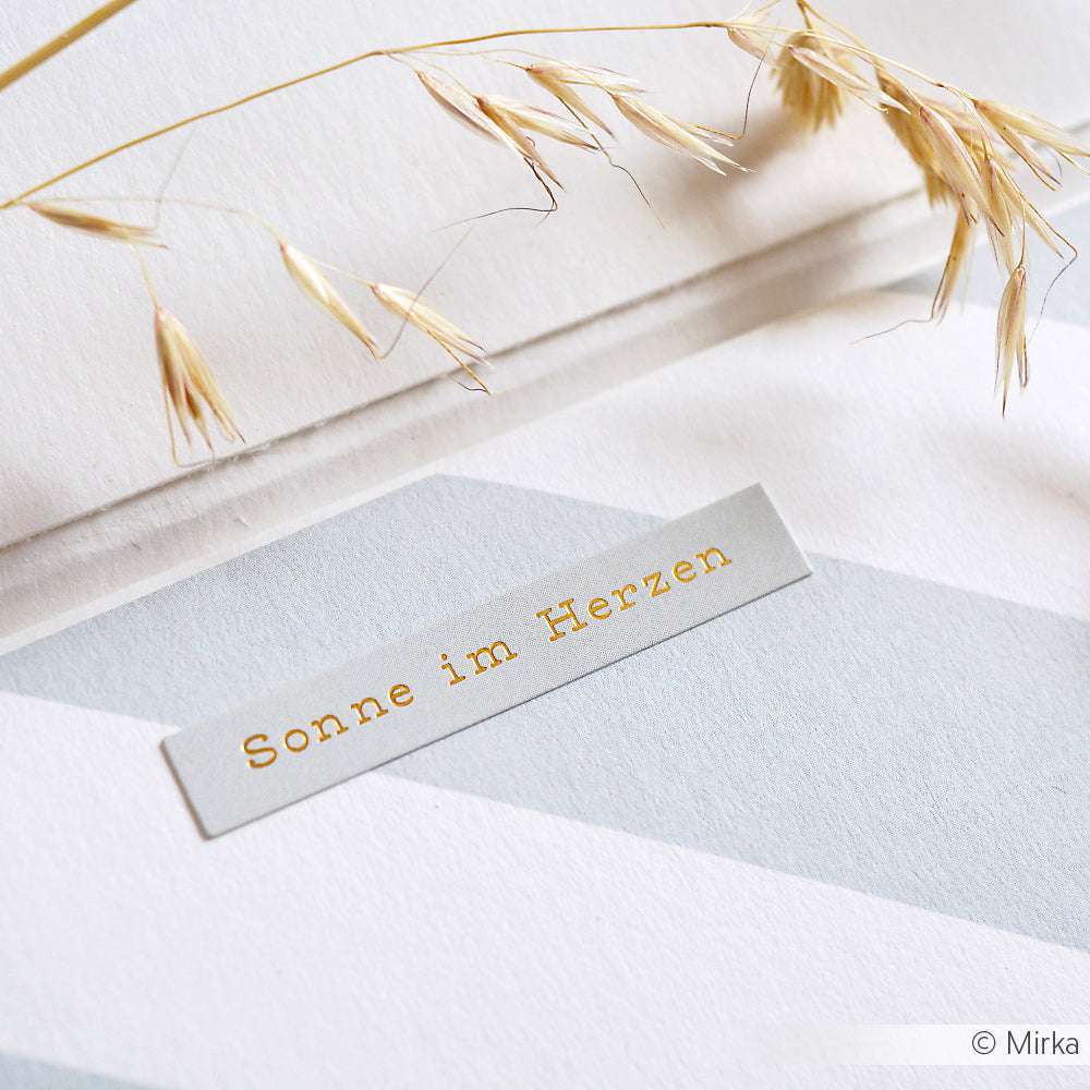 Ein Etikett mit der Aufschrift Sonne im Herzen von Alexandra Renke auf Sticker-Streifenpapier mit getrockneten Weizenhalmen darüber - ideal für kreative Kartengestaltung oder als charmantes Traumtänzer-Detail.