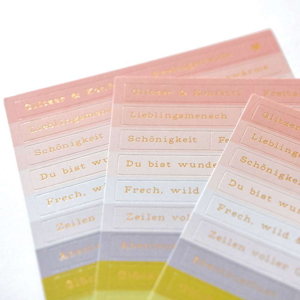Auf den pastellfarbenen Aufkleberbögen von Alexandra Renke sind deutsche Wörter und Sätze in Gold abgebildet - ideal für die Kartengestaltung oder um Ihren Bastelarbeiten einen Hauch von Glitzer & Konfetti zu verleihen.