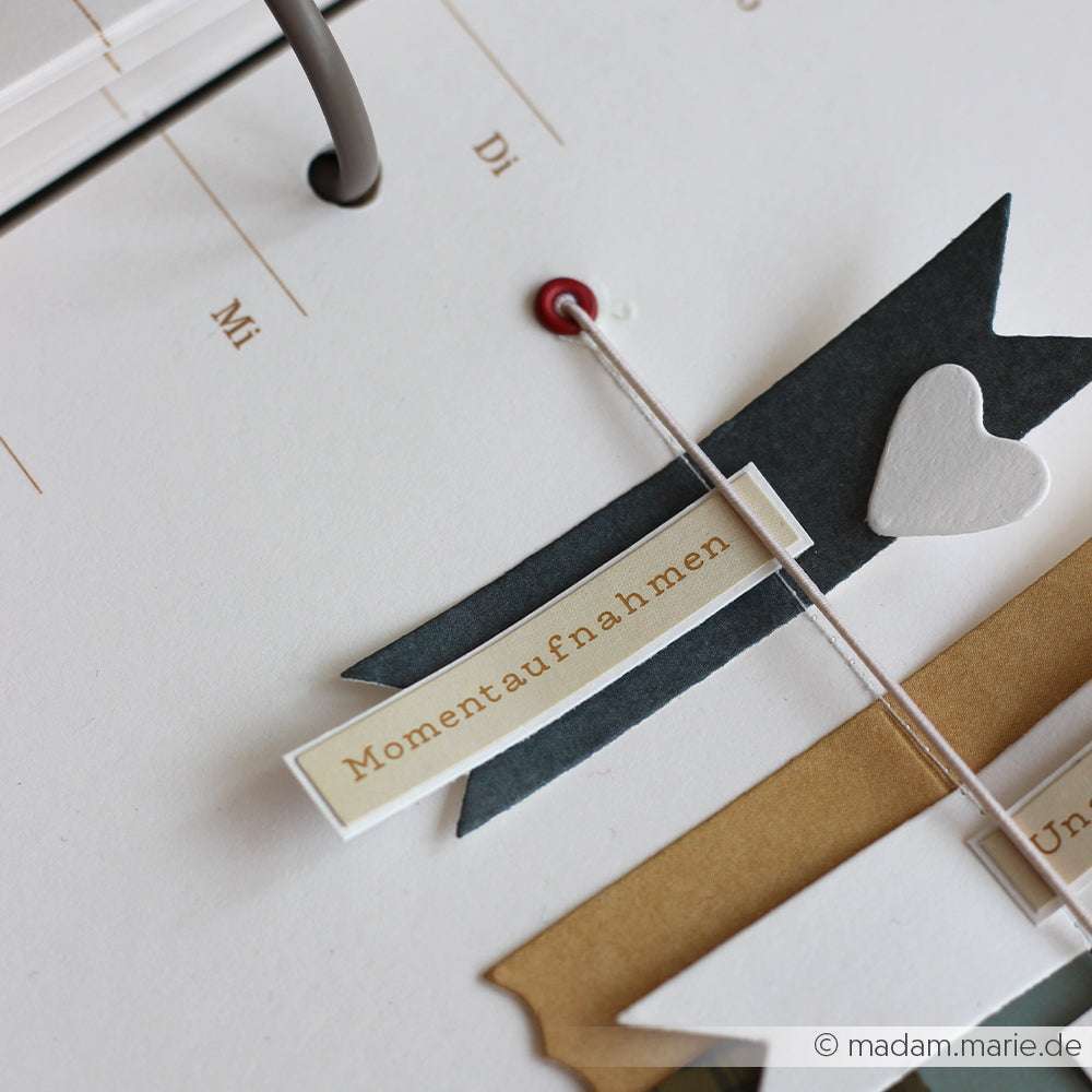 Eine Scrapbook-Seite von Alexandra Renke zeigt den Text "Momentaufnahmen" mit Herz, Banner und Sticker-Streifen - ideal für die Kartengestaltung oder um Ihren Erinnerungen einen Glitzer & Konfetti-Touch zu geben.