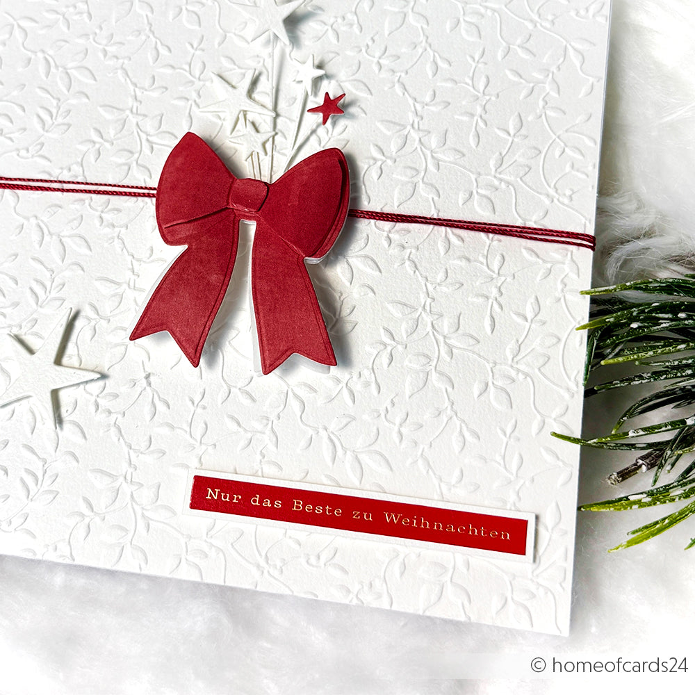 Weiße geprägte Weihnachtskarte von Alexandra Renke mit roter Schleife und "Nur das Beste zu Weihnachten" auf Deutsch. Perfekt für herzliche Grüße oder kleine Geschenke, verziert mit eleganten Aufkleberstreifen.