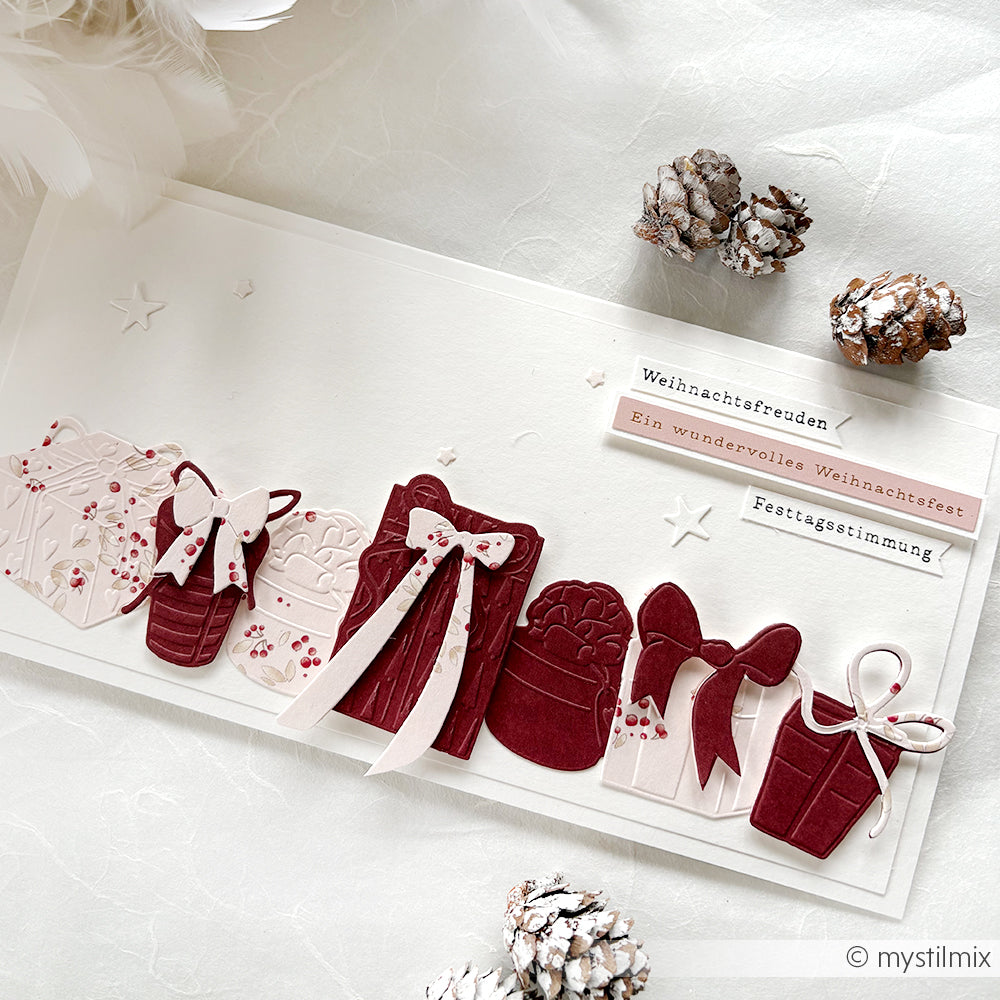 Eine handgemachte Weihnachtskarte von Alexandra Renke mit roten und weißen Geschenkausschnitten, Tannenzapfen und festlichen deutschen Grüßen - ideal für kreative Kartengestaltung und den Zauber der Weihnacht.