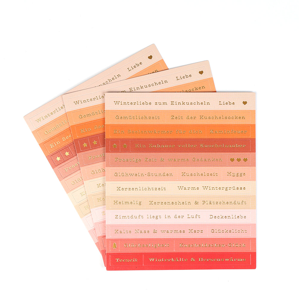 Vier Bögen mit orangefarbenen, roten und rosafarbenen Sticker-Streifen von Alexandra Renke mit kuscheligen Winterwörtern und -symbolen - perfekt für die Gestaltung von Karten oder um Ihren Bastelarbeiten einen warmen Touch zu verleihen.