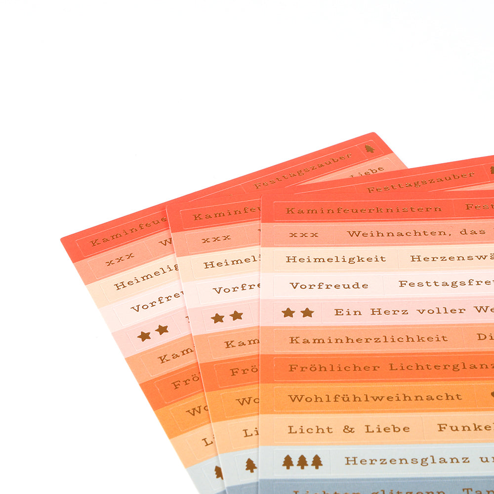 Vier Bögen mit dekorativen Etiketten von Alexandra Renke zeigen deutsche Wörter und Symbole in warmen Farbverläufen - ideal für Sticker-Streifen oder kreative Kartengestaltung, die einen Hauch von Wohlfühlweihnacht in Ihre Projekte bringen.