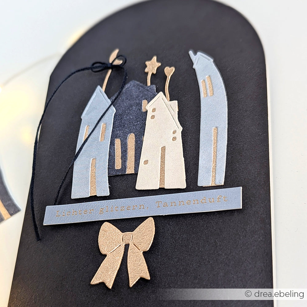 Alexandra Renke handgefertigte Karte mit metallischen Häusern, schwarzem Band, goldener Schleife und deutschem Text auf schwarz-ideal für besondere Kartengestaltung oder um Wohlfühlweihnachtsflair mit eleganten Sticker-Streifen zu bringen.