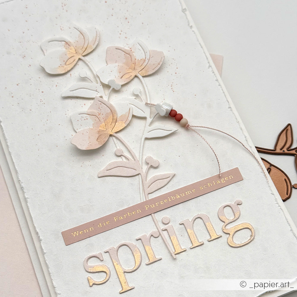 Handgemachte Frühlingskarte von Alexandra Renke mit pastellfarbenen Blumen, deutschem Text und einer Perlenschnur auf strukturiertem weißem Papier - ideal für kreative Kartengestaltung und etwas Frühlingszauber.