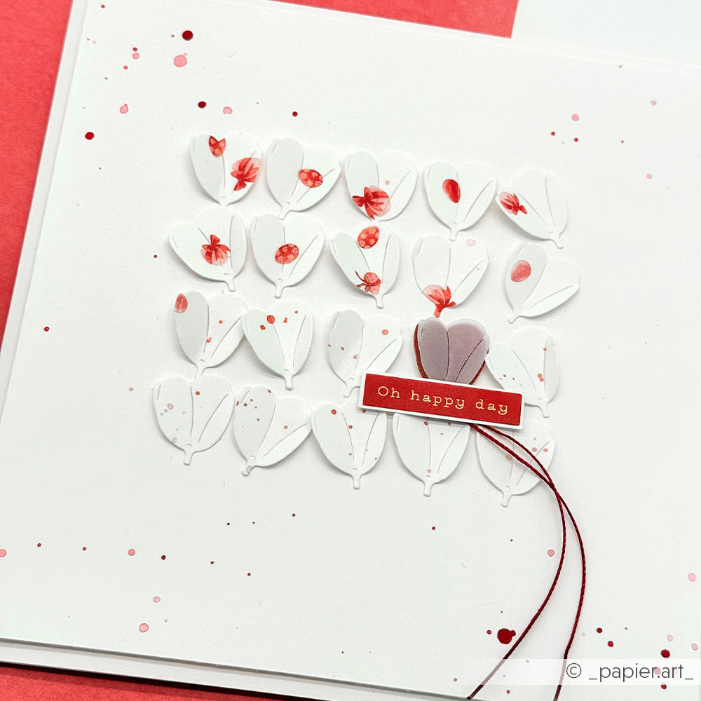 Quadratische Karte von Alexandra Renke mit geschichteten weißen Blütenblättern, roten Farbspritzern und einem roten Oh happy day Anhänger mit Schnur - ideal für kreative Kartengestaltung oder um Frühlingszauber in Ihre Grüße einzubauen.