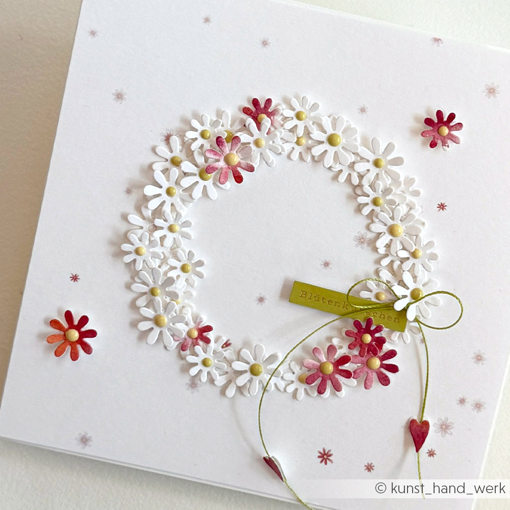 Die weiße Karte von Alexandra Renke zeigt einen Gänseblümchenkranz, rote Blumen, eine grüne Schleife und einen Anhänger - ideal für die Kartengestaltung oder um Frühlingszauber auf Ihre Sticker-Streifen zu bringen. Der klare Hintergrund bringt jedes Detail schön zur Geltung.