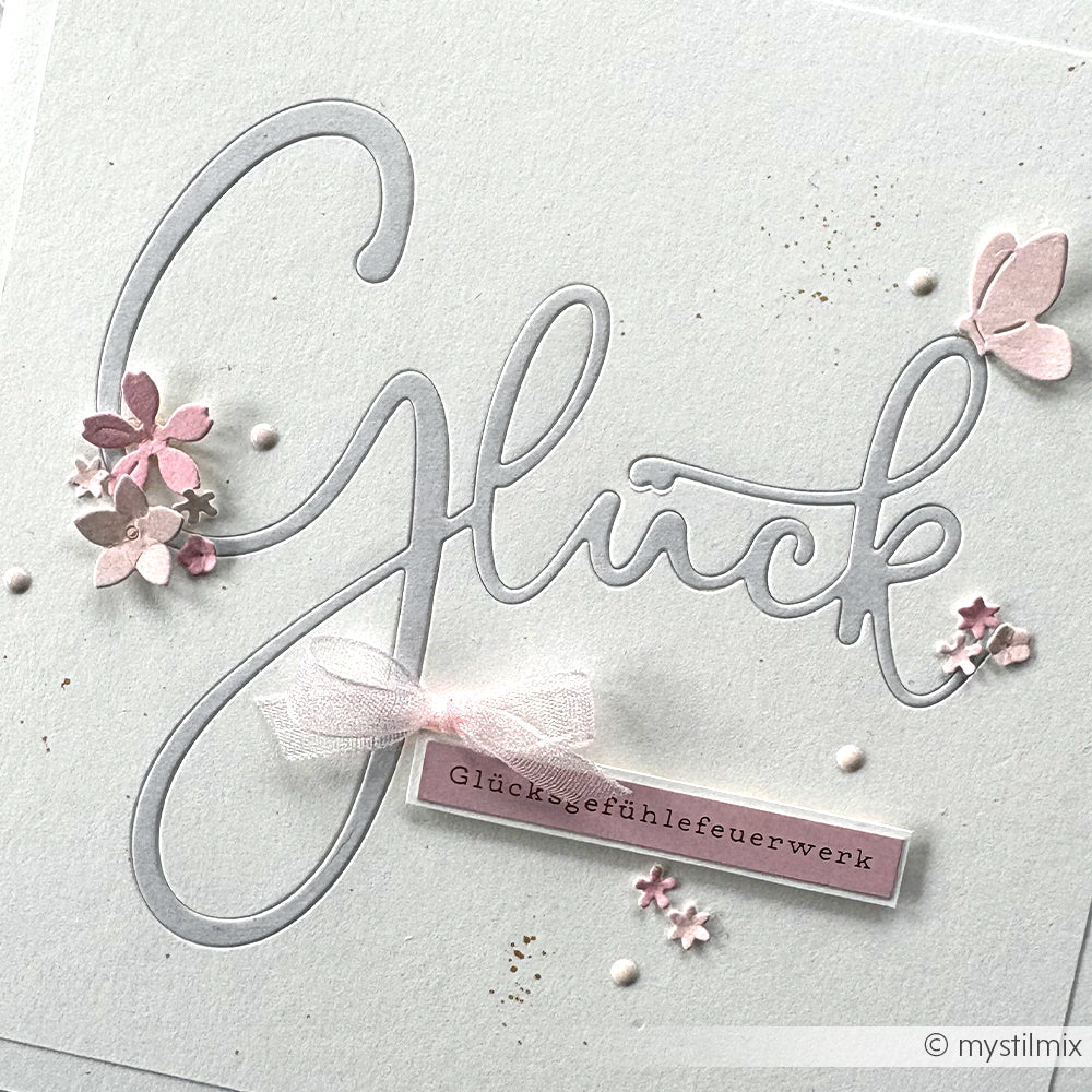 Handgefertigte Alexandra Renke Karte mit "Glück" in Schreibschrift, rosa Blumen, Schleife, Schmetterling, Sticker-Streifen-Akzenten und "Glücksgefühlefeuerwerk"-Aufkleber. Perfekt für besondere Kartengestaltung!.