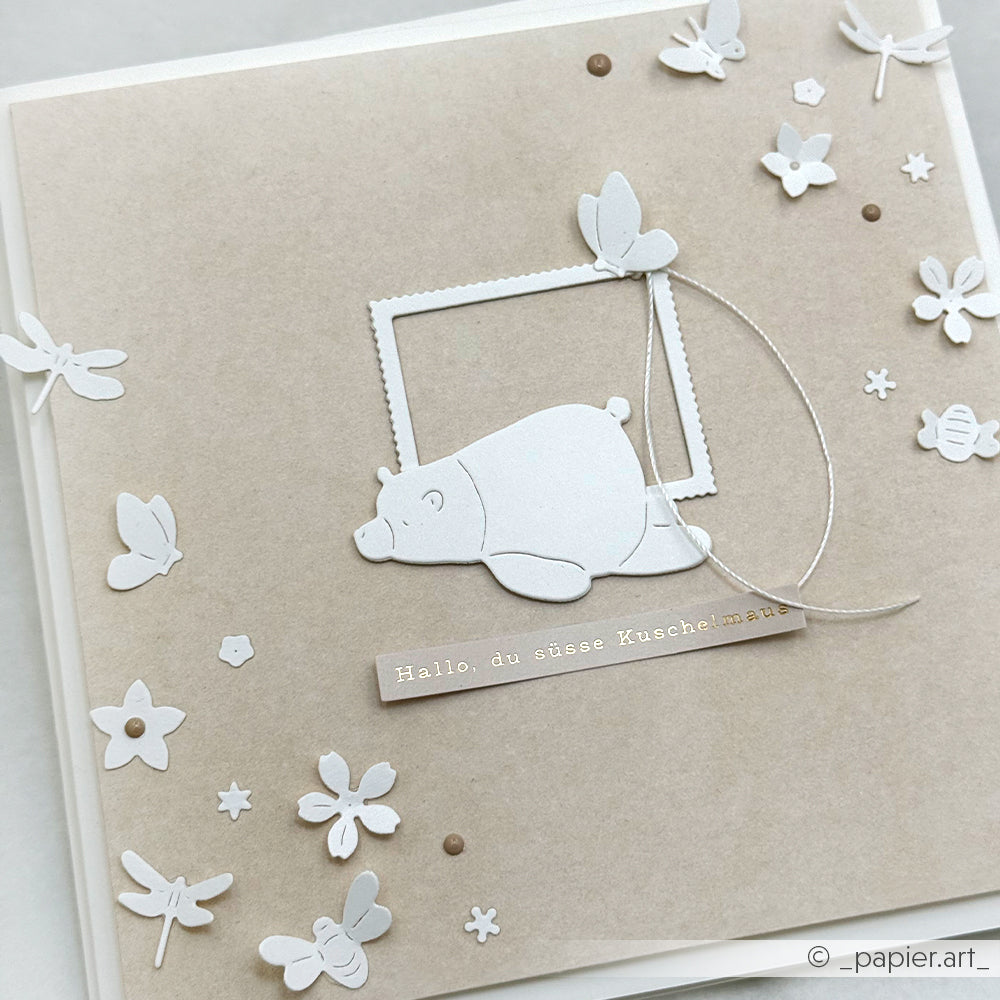 Handgefertigte Karte von Alexandra Renke mit einem weißen Bären, Schmetterlingen, Blumen und dem Text "Hallo, du süße Kuschelmaus". Perfekt zum Basteln von Karten oder zum Verzieren - mit Aufkleberstreifen und zarten Details.