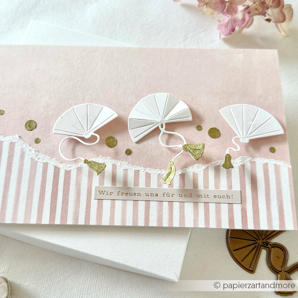 Eine handgefertigte Alexandra Renke Karte mit drei weißen Papierfächern, goldenen Akzenten und deutschem Text auf einem rosa gestreiften Hintergrund - mit Hochzeitswünsche Sticker und eleganten Sticker Streifen für eine besondere Note.