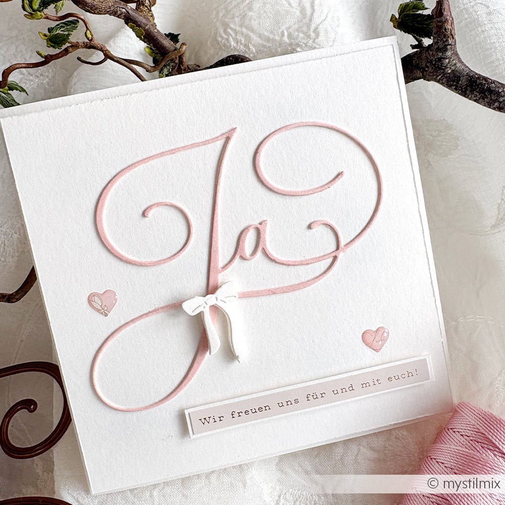 Eine weiße Alexandra Renke Karte mit "Ja" in rosa Schrift, kleinen rosa Herzen, Kartengestaltung, einer deutschen Botschaft, Hochzeitswünsche-Aufkleber und einer weißen Schleife.