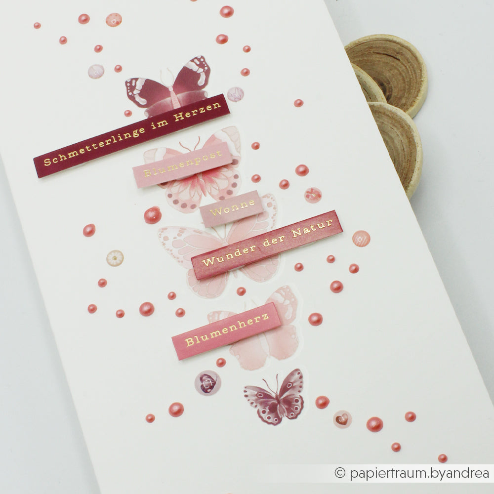 Vier rosafarbene Schmetterlinge mit deutschen Wörtern auf Etiketten flattern zwischen rosafarbenen Punkten auf Weiß - ideal von Alexandra Renke für Sticker-Streifen oder Blumenzauber in Ihren Kartengestaltungsprojekten.