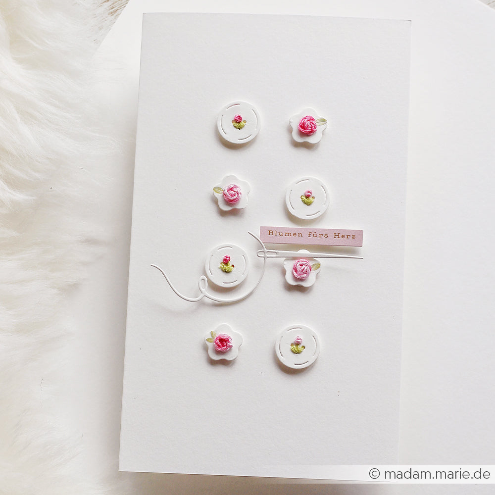 Weiße Karte von Alexandra Renke mit zartem Design und kleinen rosa und weißen 3D-Blumen. In der Mitte steht „Blumen fürs Herz“ – ein wahrer Blumenzauber für besondere Grüße.