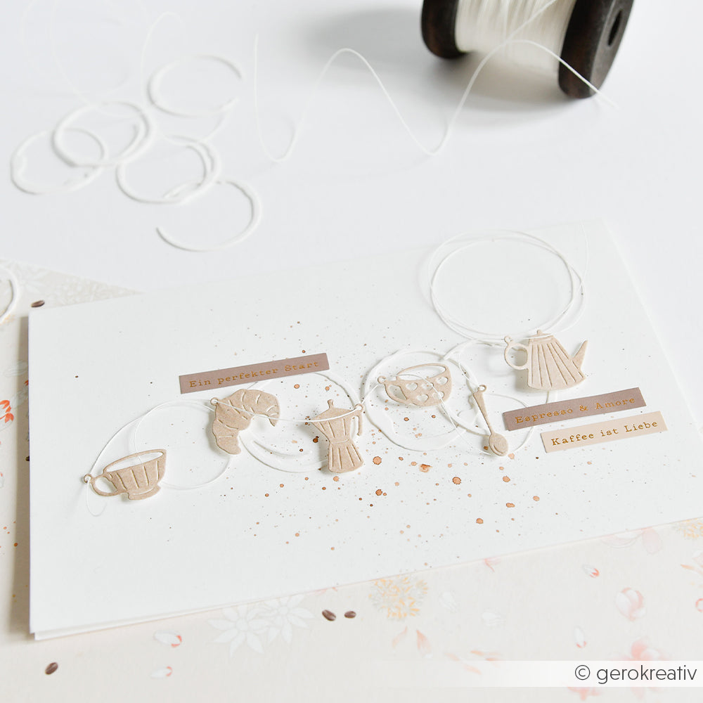 Handgefertigte Alexandra-Renke-Karte mit beigen, kaffee-inspirierten Ausschnitten und deutschem Text im „Kaffezauber“-Stil, verziert mit weißer Schnur, Aufkleberstreifen und Farbspritzern.