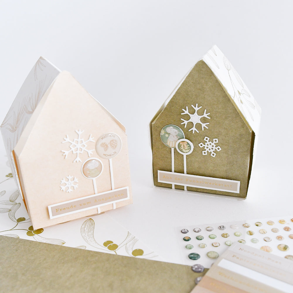 Zwei hausförmige Geschenkboxen für Weihnachtspost, verziert mit Papierschneeflocken und Aufklebern.