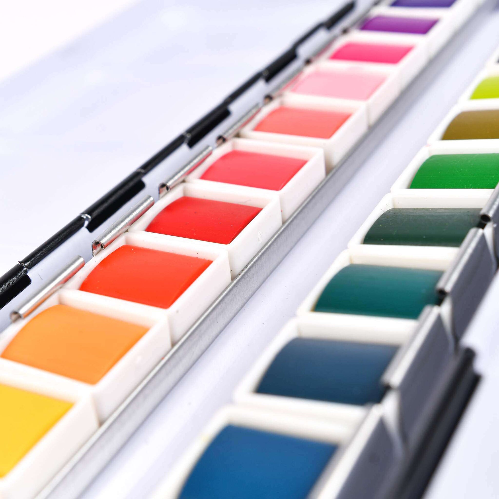 Nahaufnahme eines leuchtenden Studio Light Wasserfarben-Sets mit 24 Farben in zwei Reihen, mit einem Pinsel zwischen den Aquarellfarben-Pfännchen.