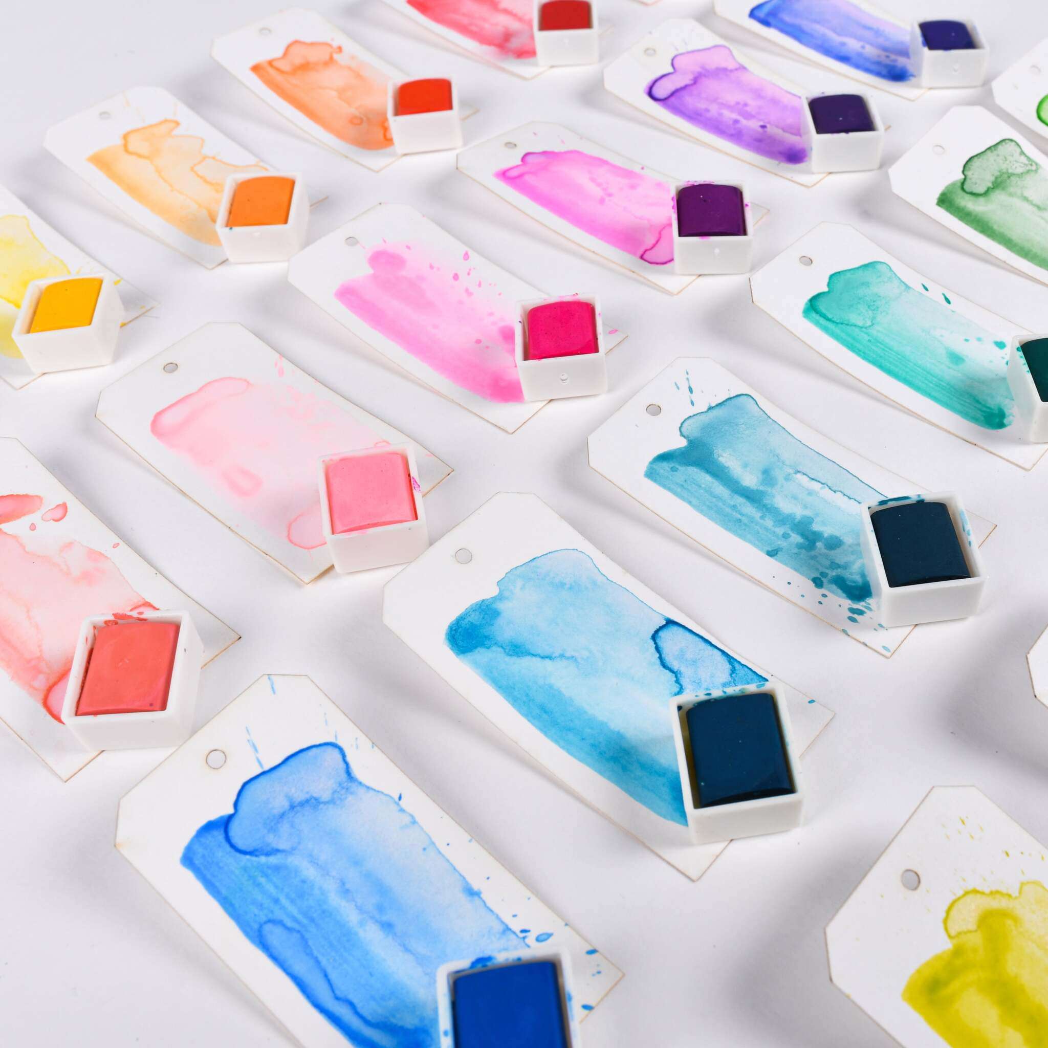 Reihen von Aquarellmustern auf Anhängern, jeweils mit einem passenden Farbtopf in leuchtenden Farbtönen aus dem Studio Light 24 Farben Wasserfarben-Set.