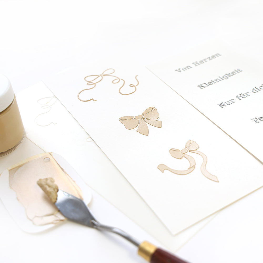 Alexandra Renke-Grußkarten mit geprägten Goldschleifen, Spachtel, Farbe und Goldpaste auf weißem Untergrund - ideal, um einzigartige Schablonen und Papierprojekte zu inspirieren.