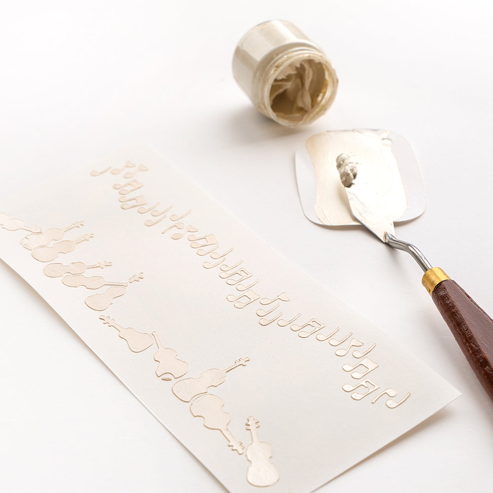 Alexandra Renke weiße Modelliermasse, Spachtel und wiederverwendbare Schablone Musterstreifen Geigenzauber mit Geigen- und Notenmotiven verzieren eine weiße Fläche.