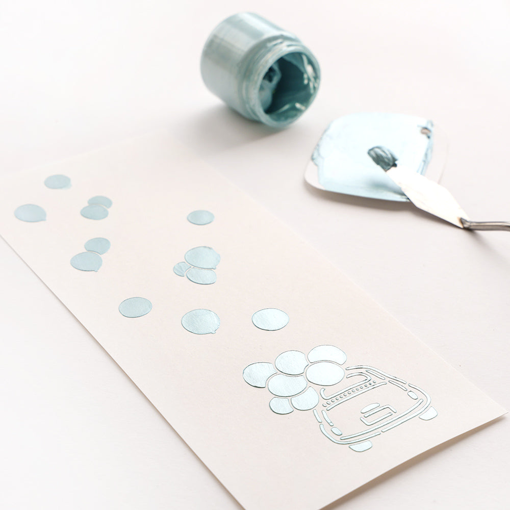 Eine hellblaue Karte mit einem Auto und Luftballons neben Kunstwerkzeugen - ideal, um wiederverwendbare Schablonen wie die Schablone Fröhliche Fahrt von Alexandra Renke für alle Ihre Schablonen für Papierprojekte zu verwenden.