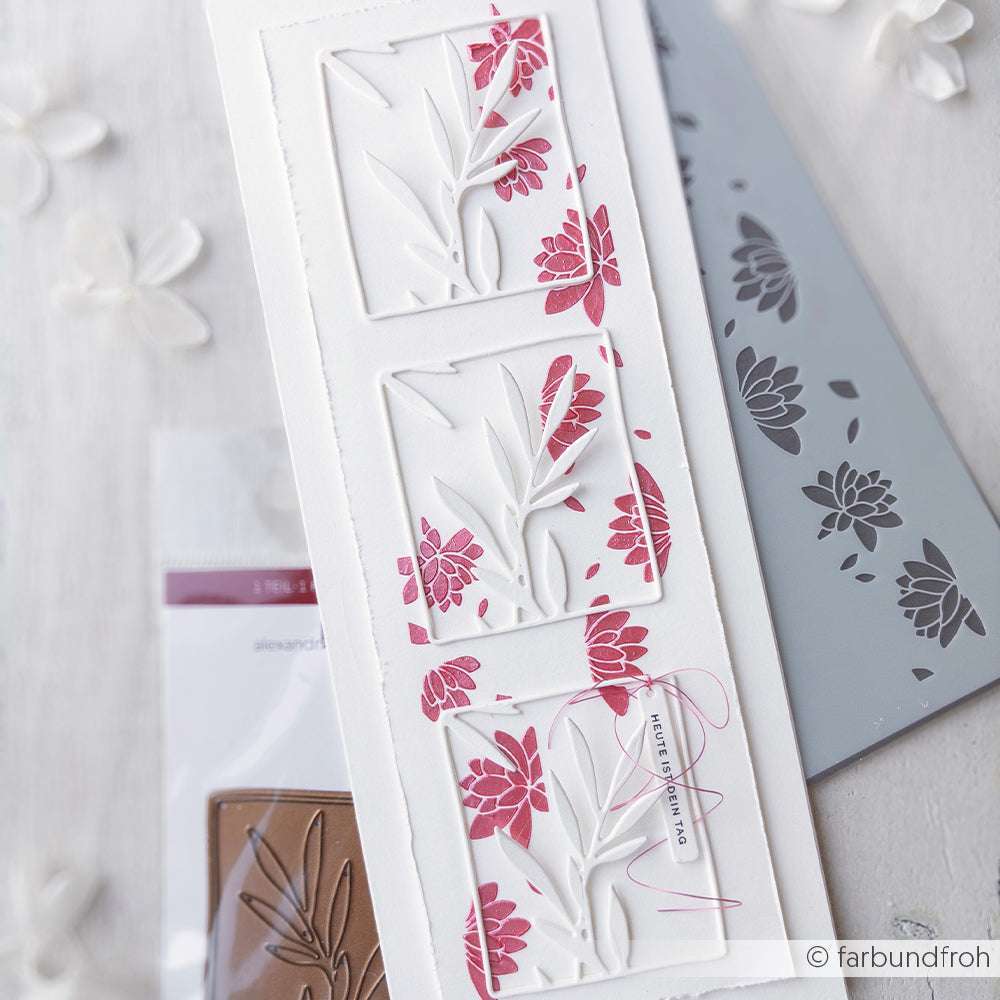 Drei weiße Karten mit roten Blumenausschnitten, die mit Alexandra Renkes wiederverwendbaren Stencils wie Stencil Blütenstreifen-Traum hergestellt wurden, sind vertikal auf einer hellen, mit Blumen akzentuierten Fläche angeordnet.