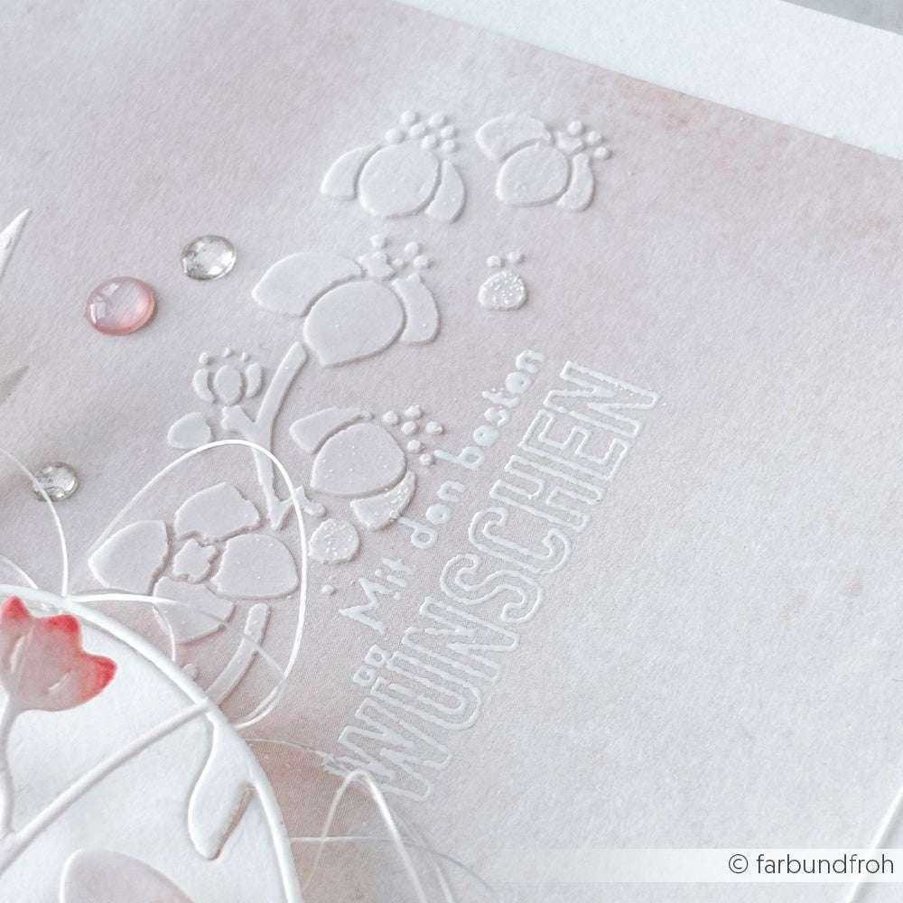 Nahaufnahme eines geprägten weißen Blumenmusters mit Alexandra Renke Blütenstreifen Stencil und "Mit den besten WÜNSCHEN" auf hellrosa Papier. Ideal für Schablonen Papierprojekte und Fans von wiederverwendbaren Stencils.