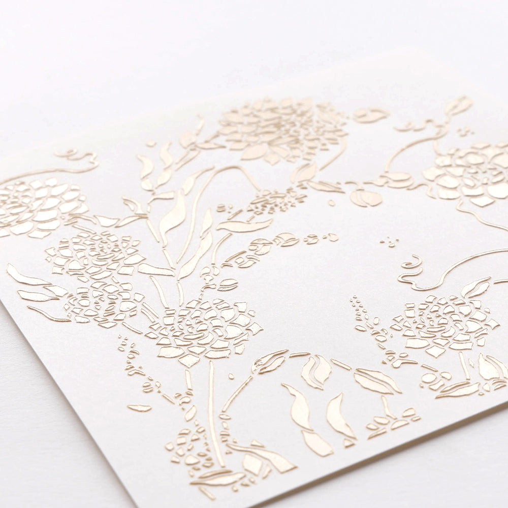 Weiße Karte von Alexandra Renke mit geprägten Dahlienwirbel-Blumenmustern in Gold, mit verschlungenen Blüten und Blättern auf einfarbigem Hintergrund, die an zarte Schablonen erinnern.