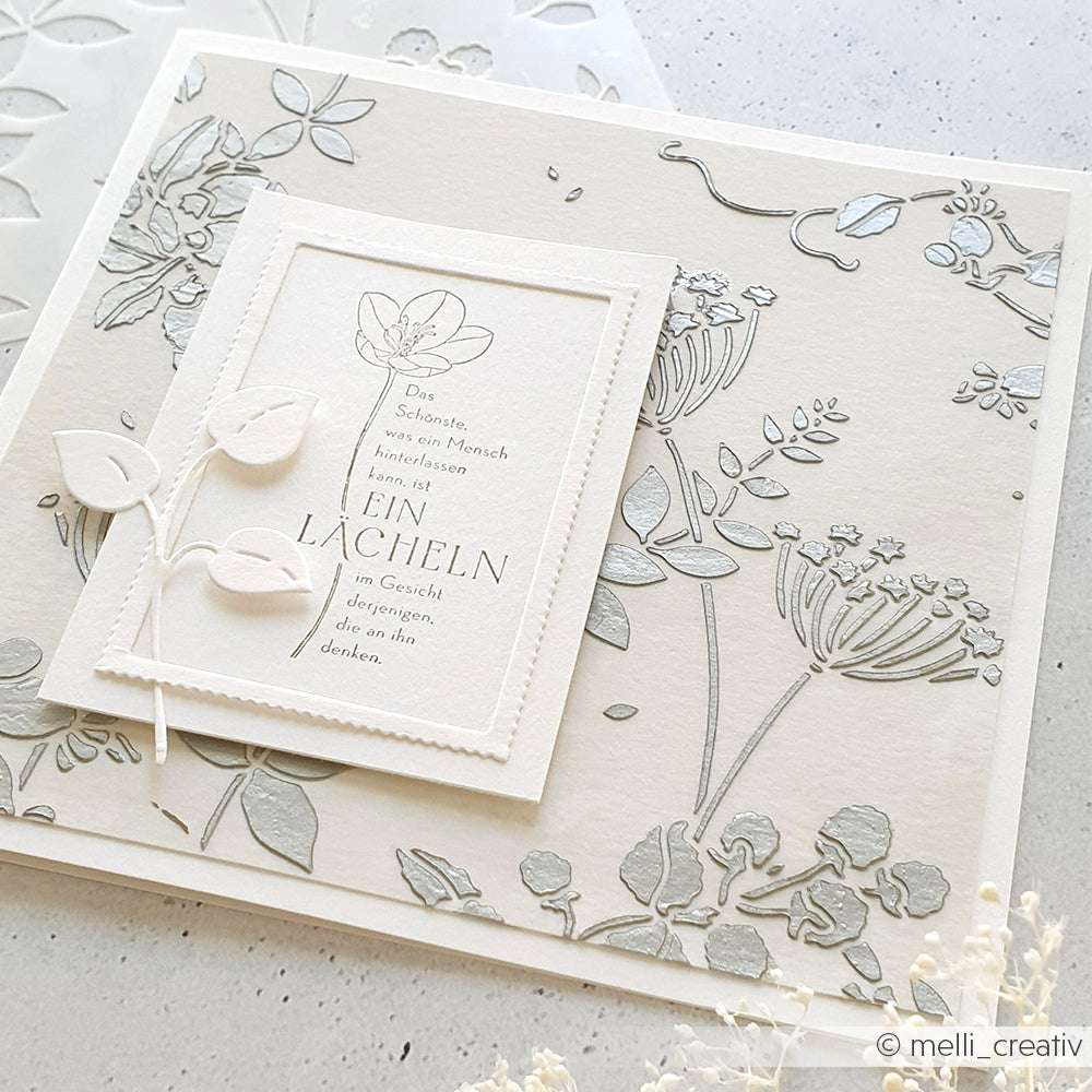 Elegante, weiß-silberne Blumenkarte von Alexandra Renke mit deutschem Text, zarten Blattakzenten und dezenten Schablonendetails auf strukturiertem Papier.