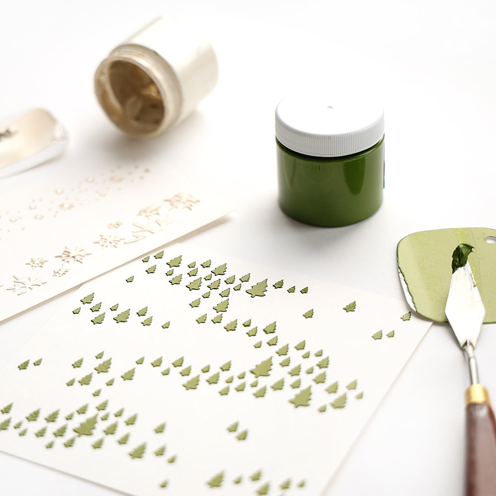 Grüner Kleister und Werkzeuge mit Alexandra Renke Papier mit kleinen grünen Bäumen schabloniert, mit Schablonen Papierprojekte und wiederverwendbare Stencil Freudige Tannenlandschaft, schaffen charmante Muster auf einer weißen Oberfläche.