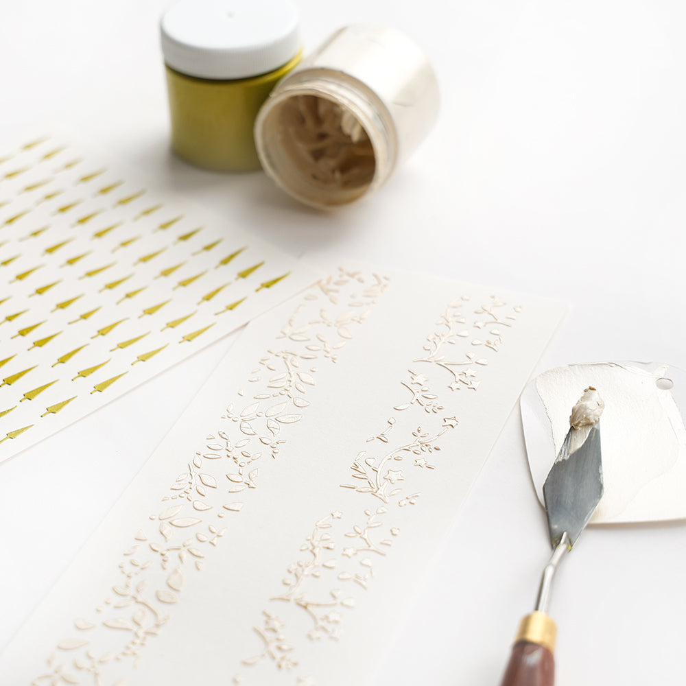 Erhabene Muster auf weißen Papierstreifen für einzigartige Papierprojekte wie Stencil Musterstreifen Ranken werden mit Alexandra Renkes Spachtel, Cremepaste und Schablonen erstellt.