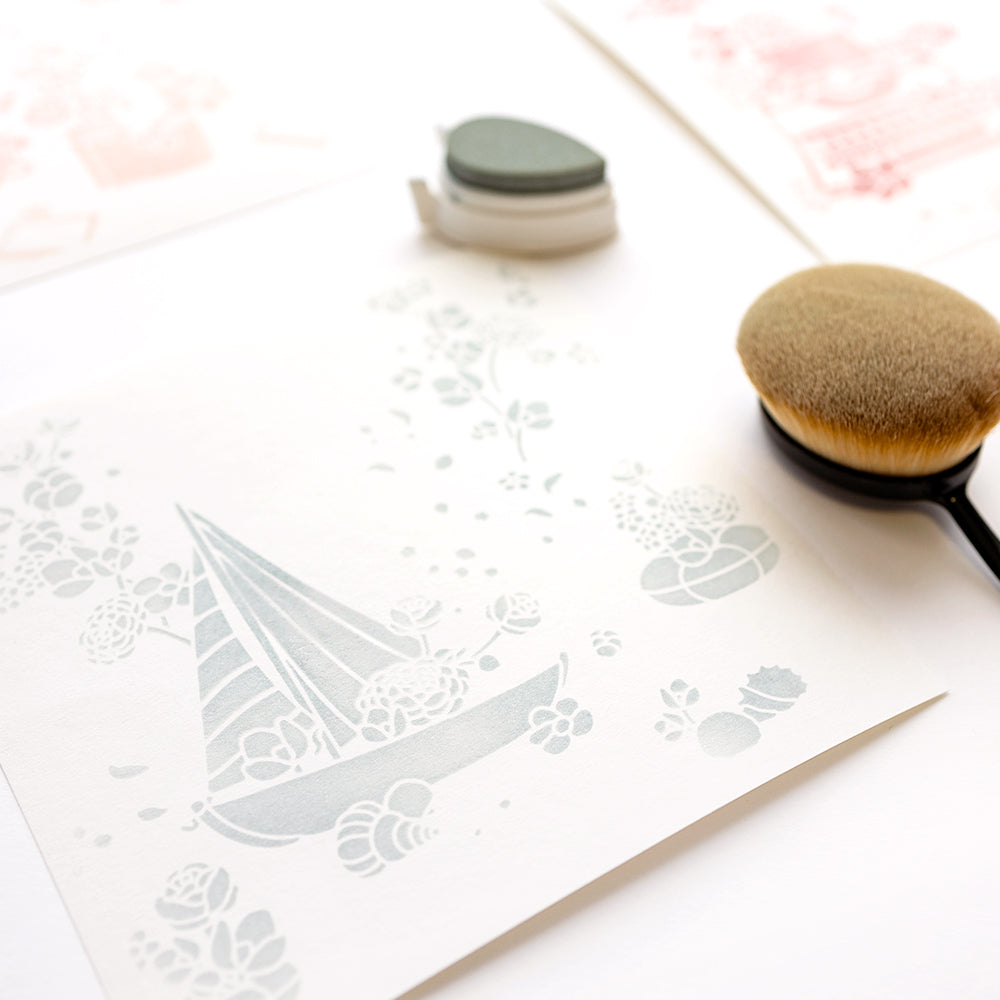 Eine zarte Pastellzeichnung eines Segelbootes auf weißem Papier, daneben ein Pinsel, ein Stempelkissen und die wiederverwendbare Alexandra Renke Schablone Meereswirbel für Ihre Schablone Papierprojekte.