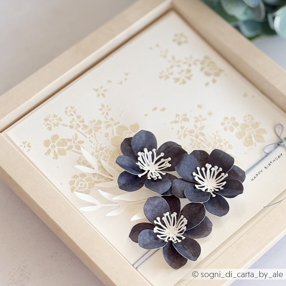 Handgefertigte Geburtstagskarte mit drei schwarzen Papierblumen und einem zarten beigen Blumenhintergrund, gestaltet mit Schablonen von Alexandra Renke für zusätzliche Details und verpackt in einer beigen Schachtel. Das Schablonendesign „Fotowirbel“ von Alexandra Renke ist wiederverwendbar und eignet sich daher perfekt, um jedes Mal elegante und einzigartige Karten zu gestalten.