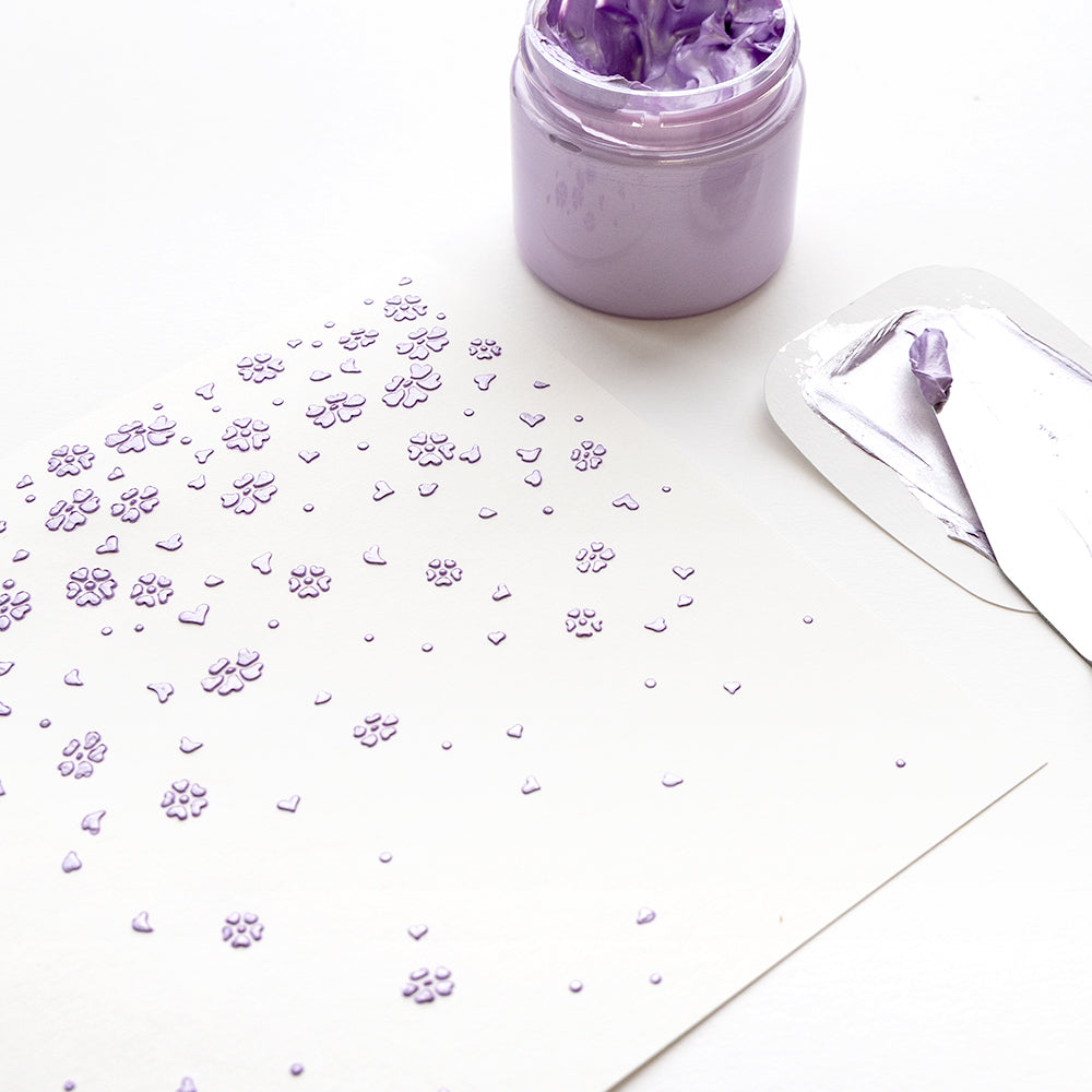 Ein Spachtel, fliederfarbener Kleister und strukturierte fliederfarbene Blumen und Herzen auf weißen Schablonen Papierprojekten mit Alexandra Renke wiederverwendbare Stencils schaffen einen charmanten Stencil Herzblütenfall-Effekt.