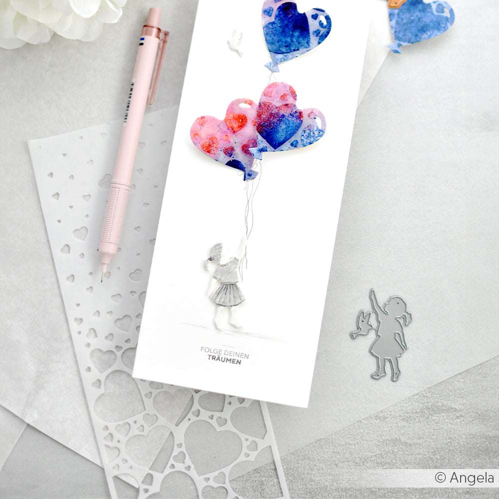 Handgemachte Karte von Alexandra Renke mit einem Mädchen, das herzförmige Luftballons in der Hand hält, neben einem Stift und einer unserer vielseitigen Schablonen.
