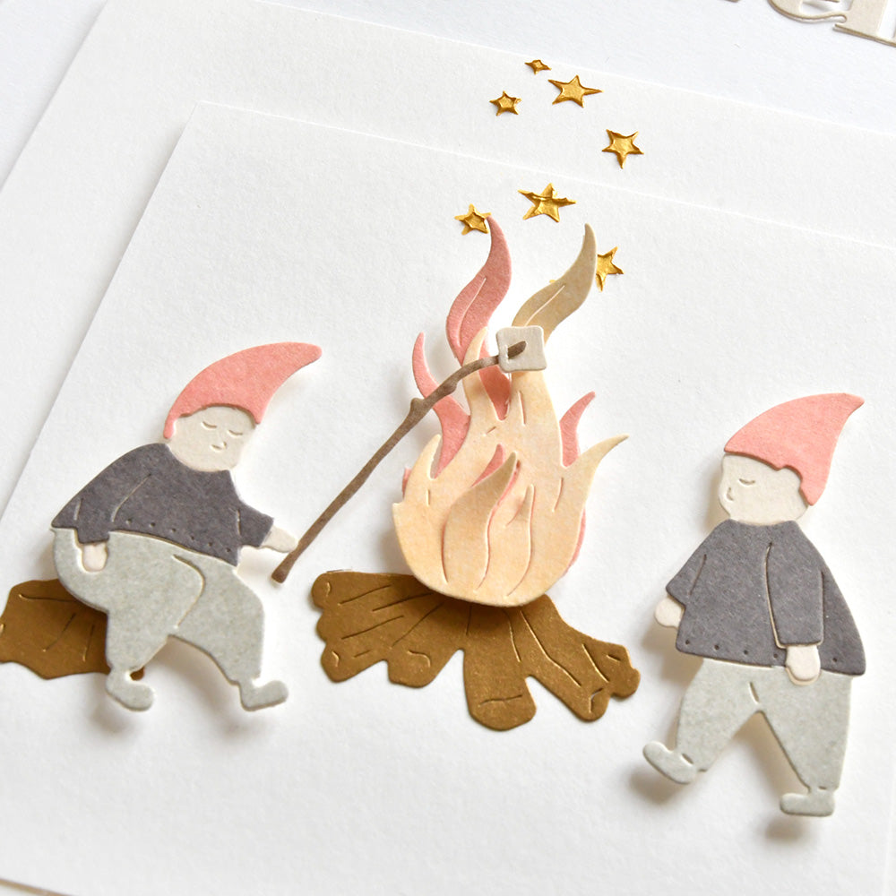 Die Schablonen-Zwerge von Alexandra Renke rösten Marshmallows am Lagerfeuer unter goldenen Sternen, perfekt für Schablonen Papierprojekte. Diese bezaubernden Designs heben sich auf einem strahlend weißen Hintergrund ab.
