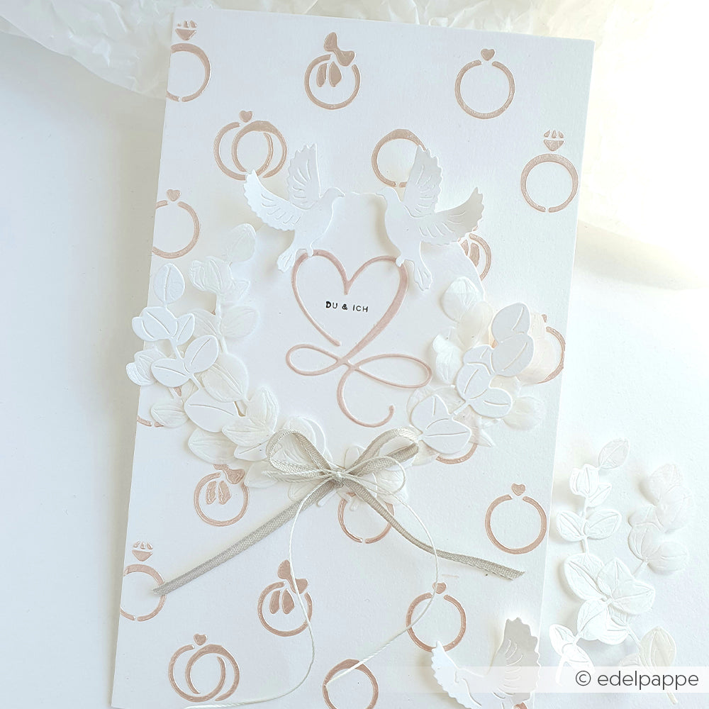 Weiße Hochzeitskarte von Alexandra Renke mit geprägten Ringen, zwei Tauben, einem Herz, einem Blumenkranz und einer silbernen Schleife - ideal für elegante Papierprojekte oder zum Setzen stilvoller Akzente mit Ihrer Lieblingsschablone.
