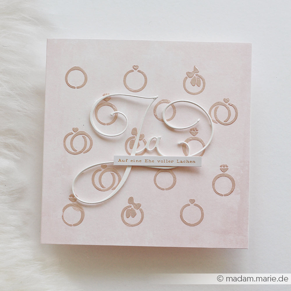 Quadratische Hochzeitskarte von Alexandra Renke mit goldenen Ringen, kursivem "Ja" und dem deutschen Text "Auf eine Ehe voller Lachen" - ideal für Papierprojekte oder zum Gestalten mit Schablonen.