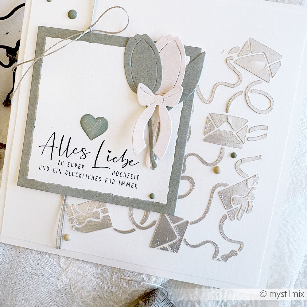 Handgefertigte Hochzeitskarte von Alexandra Renke mit deutschem Text, Herz, Blume, Schleife und silbernem Umschlag auf weißem Hintergrund, hergestellt mit wiederverwendbaren Stencils für Schablonen Papierprojekte und Stencil Verschlungene Liebesbriefe.