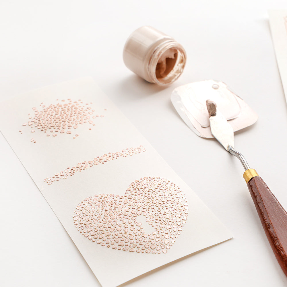 Ein Spachtel, Kleister und Papier mit strukturierten Punkten, die ein Herz und Linien auf einer weißen Oberfläche bilden, erstellt mit Alexandra Renke Produkten für kreative Designs.