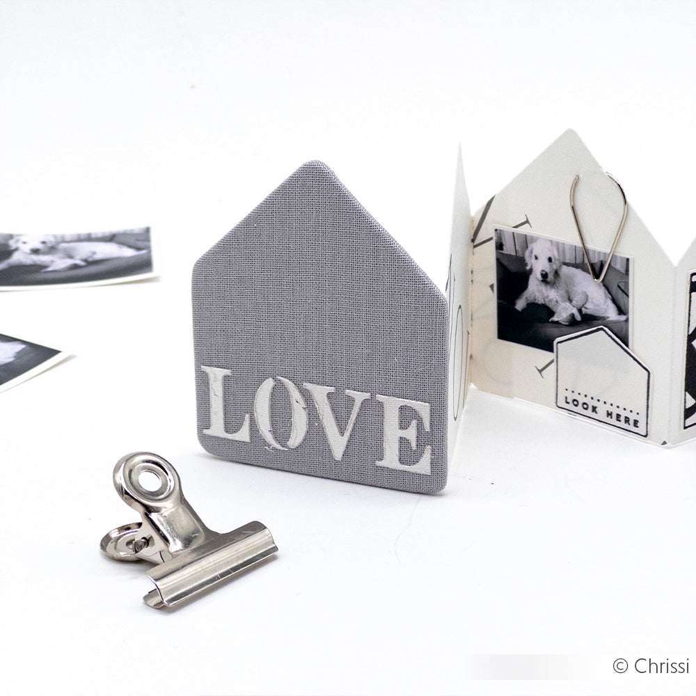 Das graue Hausdekor mit LOVE-Schriftzug von Alexandra Renke verfügt über ein Fotoalbum, eine Metallklammer und schwarz-weiße Hundefotos - perfekt, um Erinnerungen zu präsentieren und Papierprojekte mit Schablonen oder Schablonen in Szene zu setzen.