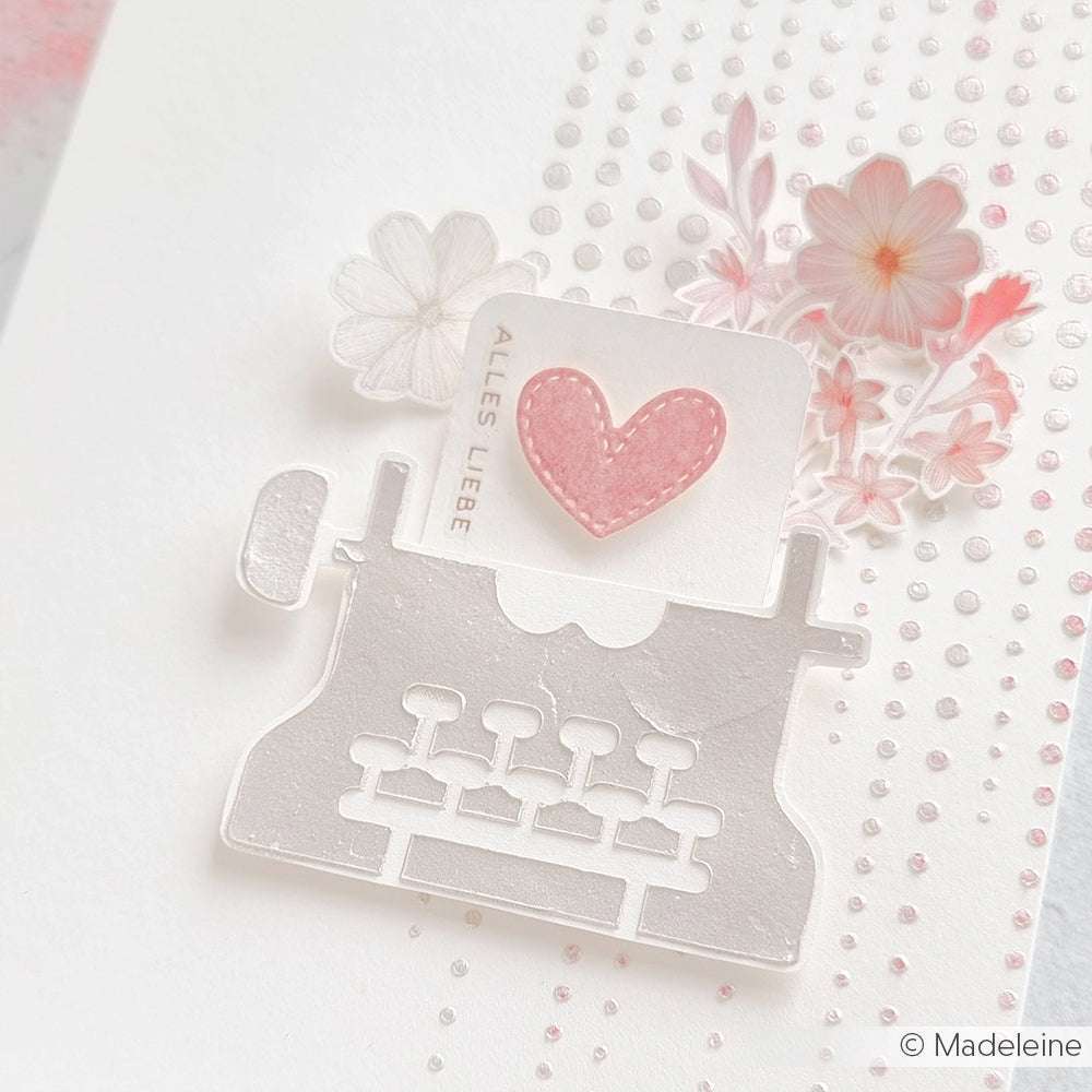 Die weiße Papierschreibmaschine von Alexandra Renke ist mit einem rosafarbenen Herz, floralen Akzenten und einer "ALLES LIEBE"-Karte versehen - ideal für Papierprojekte oder zum Verzieren von Schablonen-Basteleien.