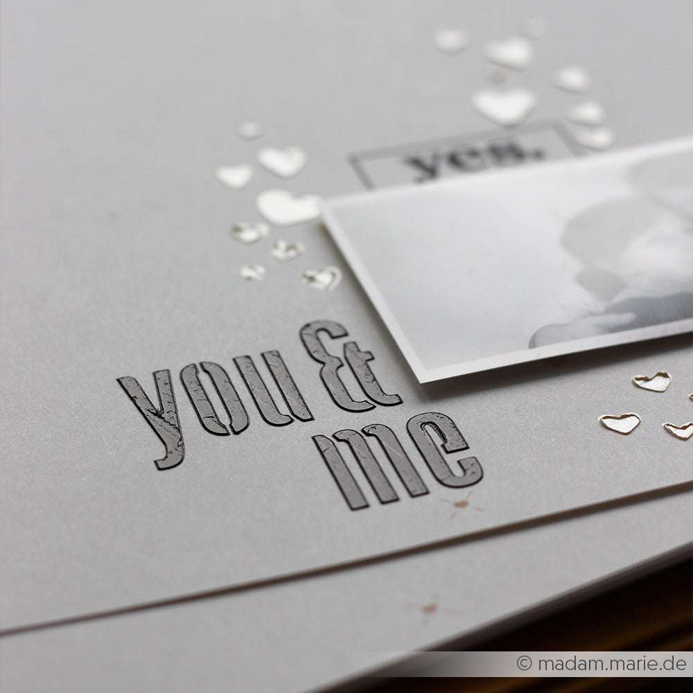 Eine Graustufenkarte von Alexandra Renke mit dem Text "you & me", kleinen erhobenen Herzen, einem teilweise sichtbaren Foto und zarten Schablonenakzenten.